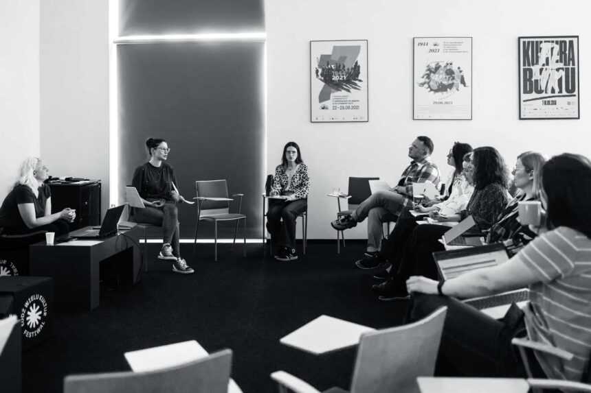 Grupa osób siedząca w kręgu na krzesłach w dużej sali