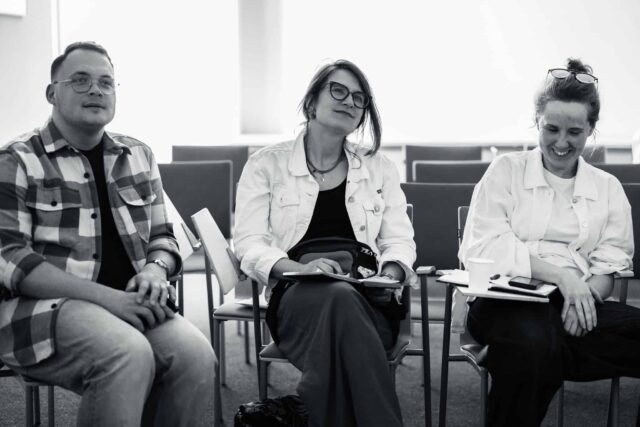 Dwie kobiety i mężczyzna siedzący w rzędzie na krzesłach w sali