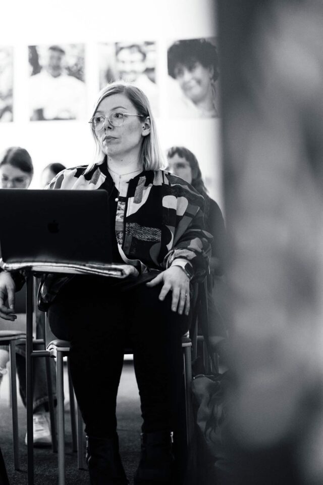 Kobieta siedząca w sali, przed nią laptop