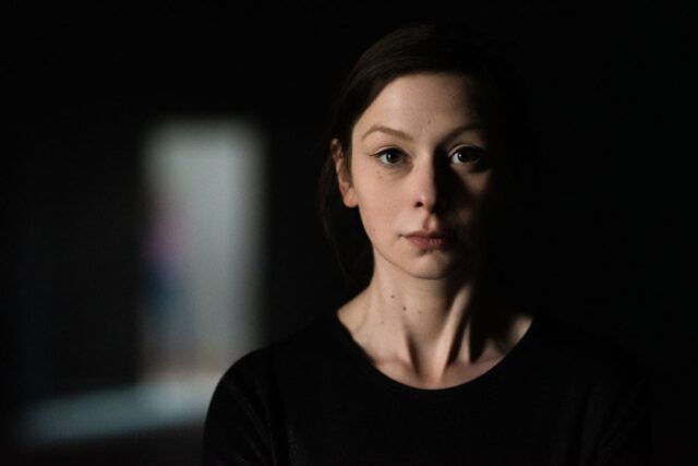 Kobieta ubrana na czarno w ciemnym pomieszczeniu patrząca w obiektyw