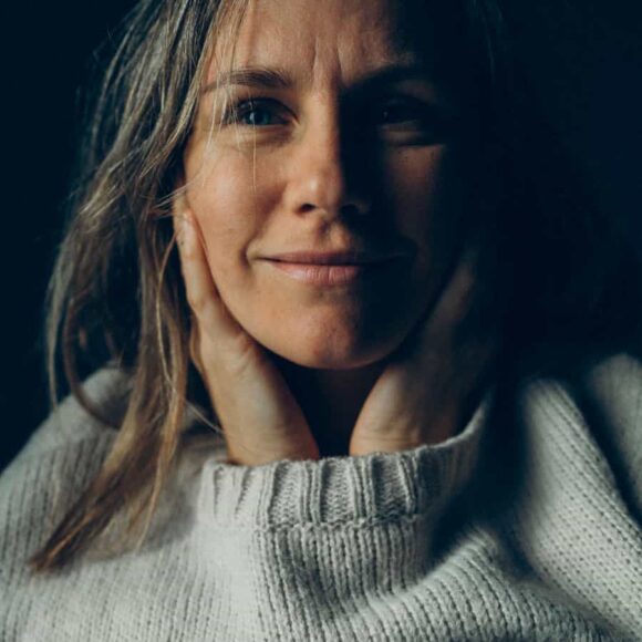 Kobieta w grubym swetrze z dłońmi przy twarzy