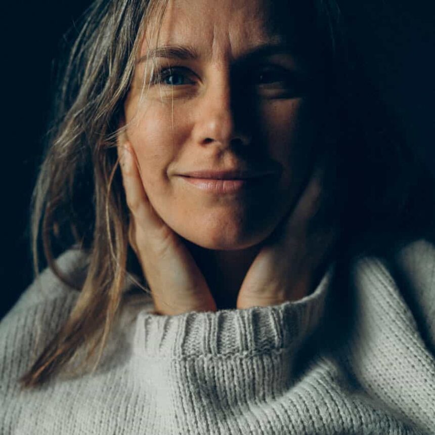 Kobieta w grubym swetrze z dłońmi przy twarzy