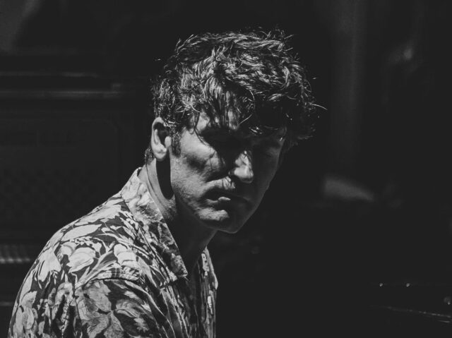 Mężczyzna w koszuli w kwiaty z zamkniętymi oczami, oświetlony punktowo