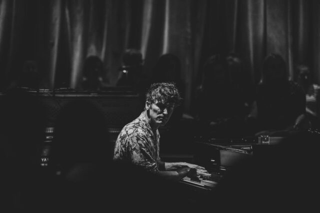 Mężczyzna grający na fortepianie podczas koncertu, w tle widownia.