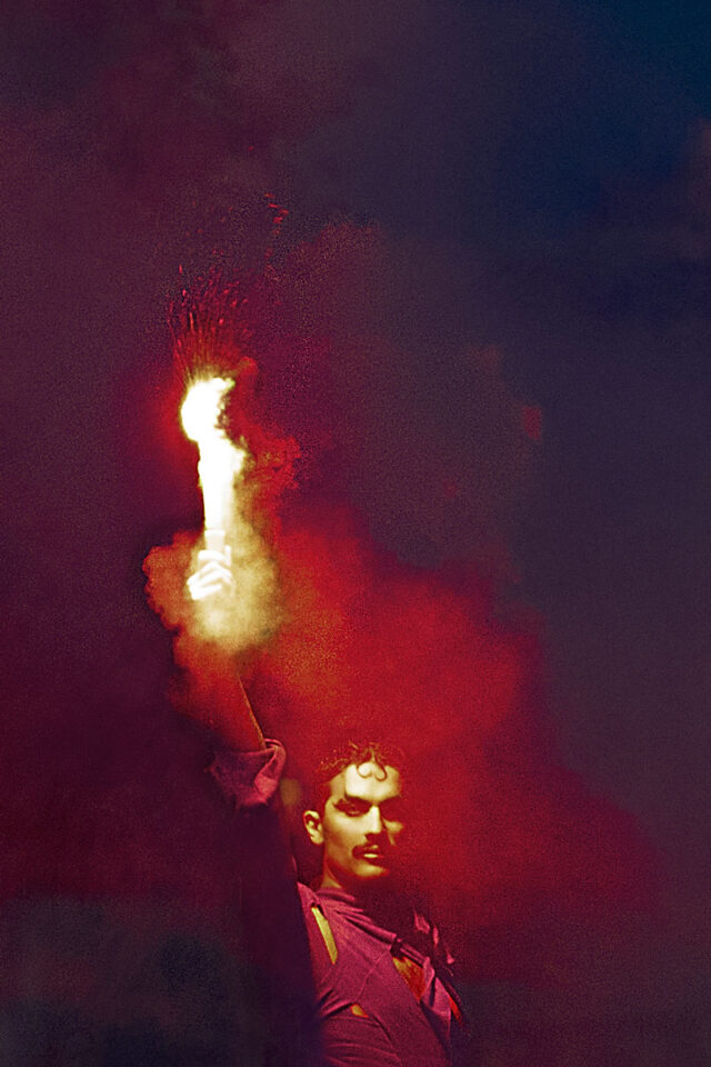 Mężczyzna w trakcie performansu z ogniem w dłoni na czarnym tle