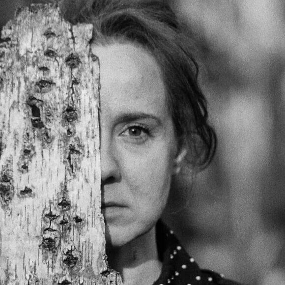 Kobieta ukrywająca pół twarzy za korą drzewa