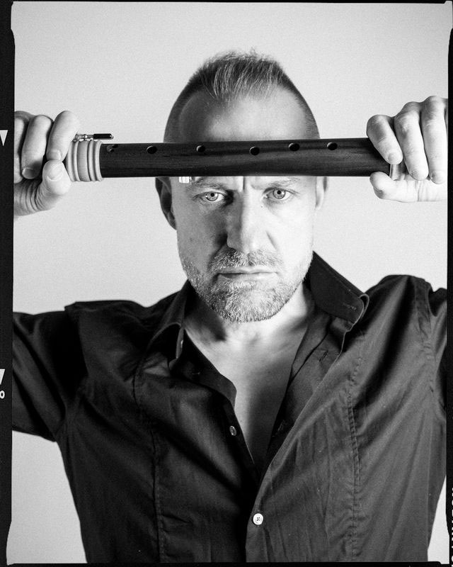 Czarno-białe zdjęcie portretowe mężczyzny trzymającego flet przy czole