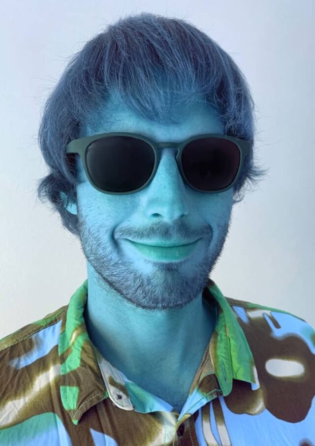 Młody usmiechnięty męzczyzna w czarnych okularach, w niebieskim świetle