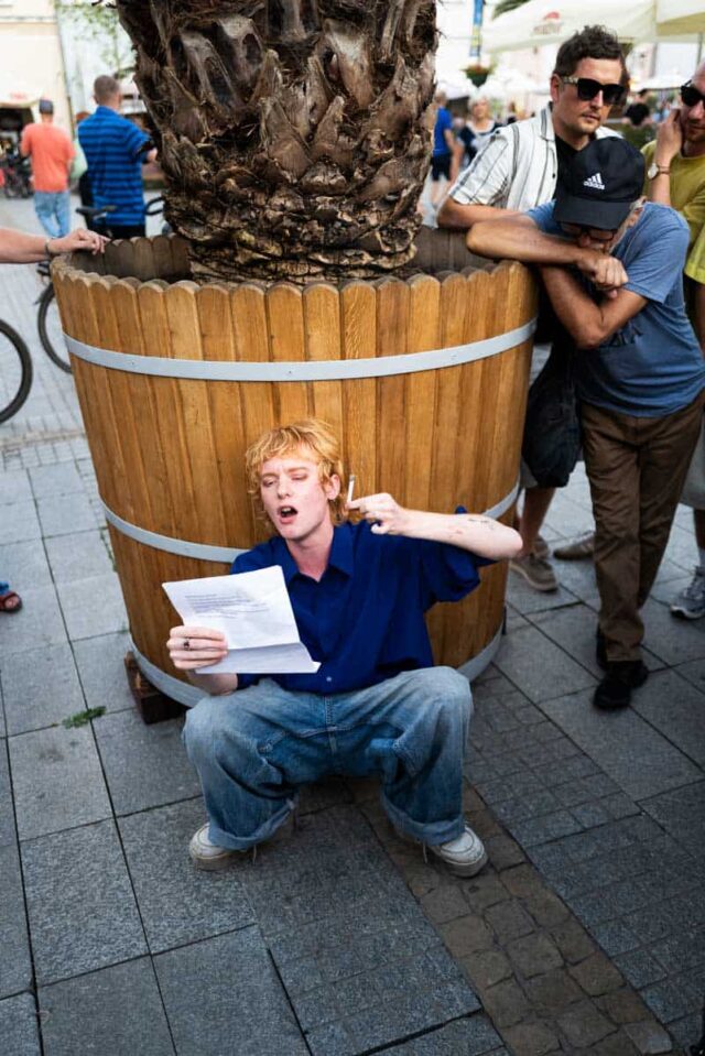 Młody mężczyzna z kartką kuca na ulicy