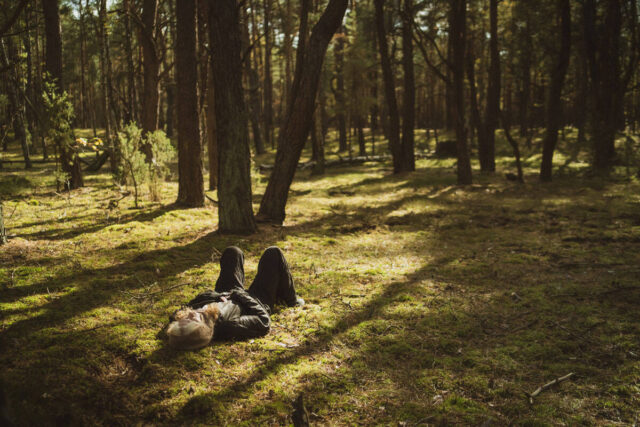 Postać leżąca na trawie w lesie