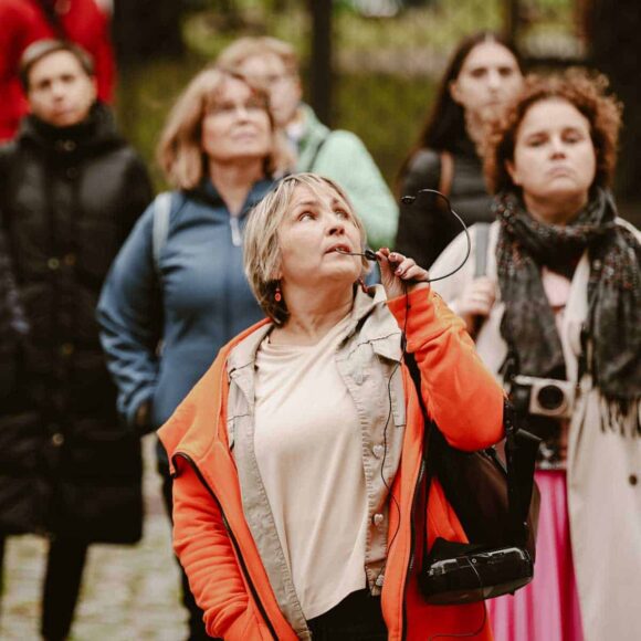 Kobieta oprowadzająca wycieczkę z mikrofonem patrząca do góry, ludzie w tle