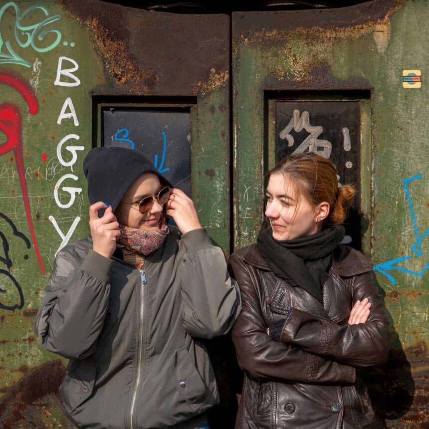 Dwie nastolatki siedzą na tle ściany z graffiti i patrzą na siebie