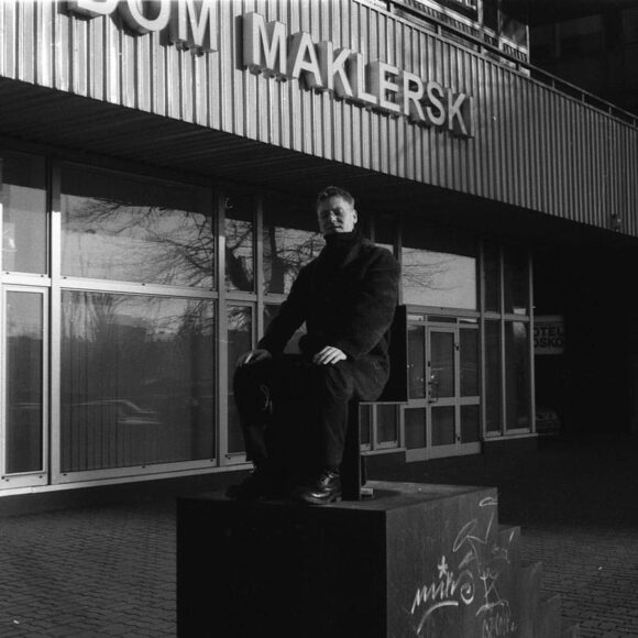 Męzczyzna w czarnym płaszczu siedzi na rzeźbie przed domem maklerskim