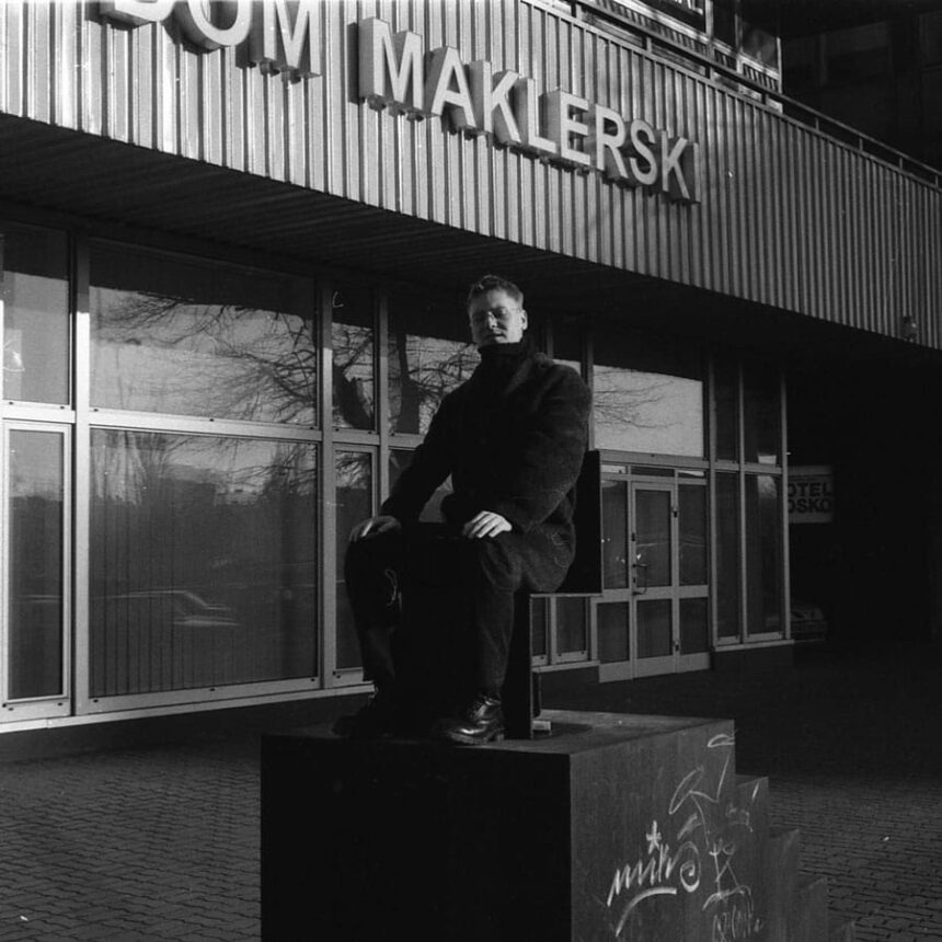 Męzczyzna w czarnym płaszczu siedzi na rzeźbie przed domem maklerskim