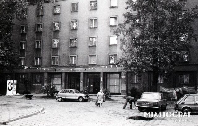 budynek akademika, przed nim auta i 2 osoby, archiwalne zdjęcie