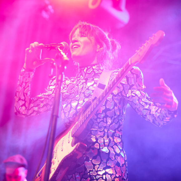 Kobieta w świecącym stroju z gitarą przy mikrofonie