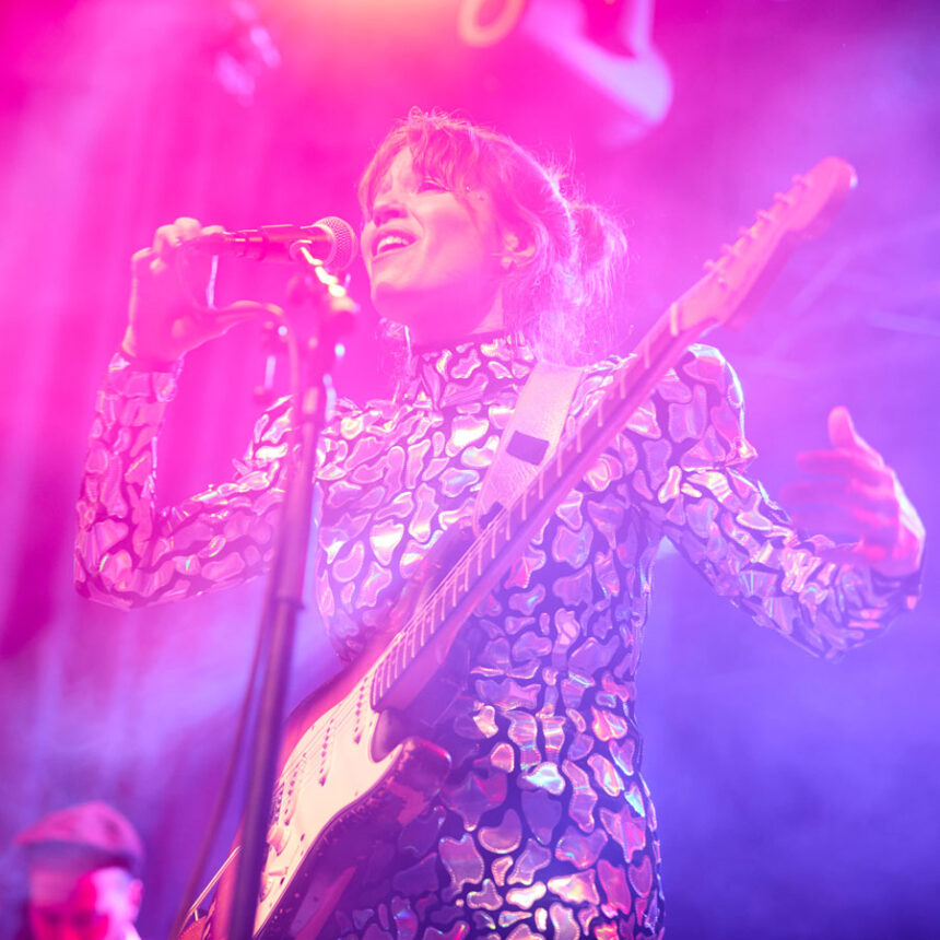 Kobieta w świecącym stroju z gitarą przy mikrofonie