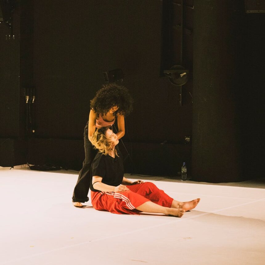 Jedna kobieta stoi nad druga siedzącą, trzyma jej głowę