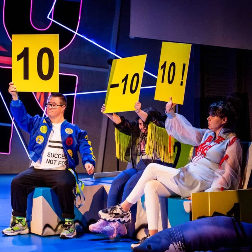 3 osoby jurorskie kolorowo ubrane z podniesionymi tabliczkami z punktacją 10, -10, 10!