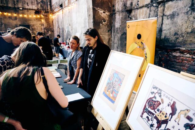 Grupa osób przy stoisku z rycinami w ramach