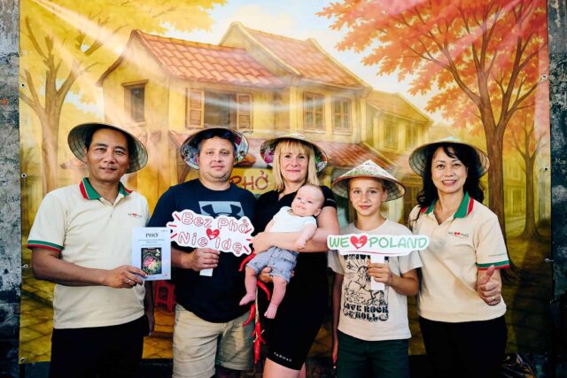 Grupa osób w wietnamskich nakryciach głowy na tle plakatu