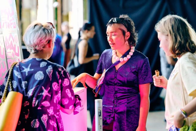 Młoda kobieta z oryginalnym artystycznym makijażem na twarzy rozmawia z kobietami stojącymi tyłem