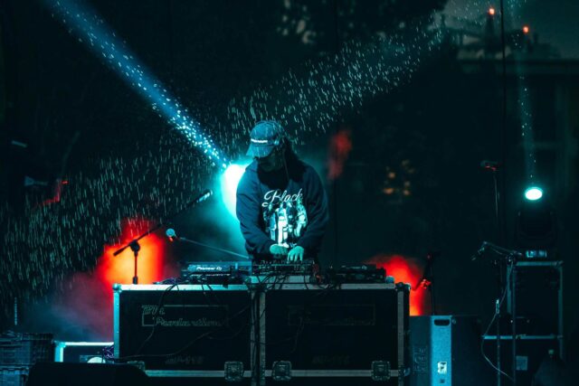 DJ w czarnej bluzie i czapce gra w nocy na scenie w deszczu