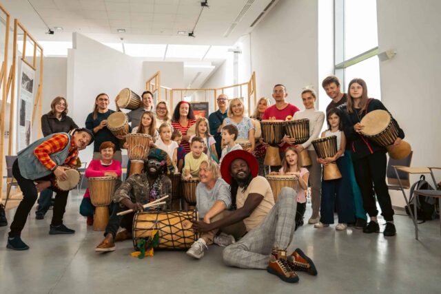 Grupa kilkudziesięciu osób z bębnami w jasnym wnętrzu