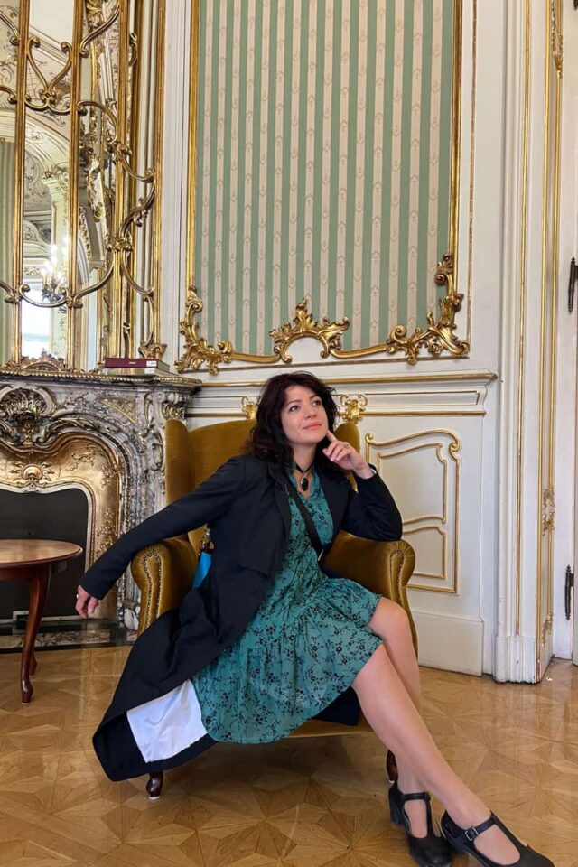 Kobieta w zielonej sukience siedzi we wnętrzu pałacowej sali