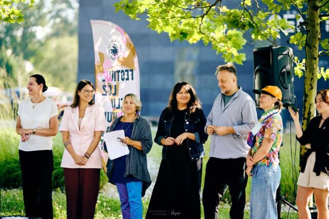 Grupa 7 osob w tle flaga Festiwalu i budynek