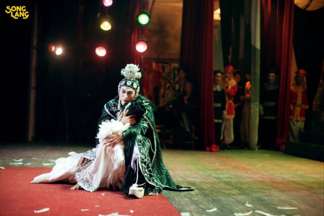 Na pierwszym planie dwie osoby na scenie, (jedna przytrzymuje drugą) w tle ludzie za kulisami