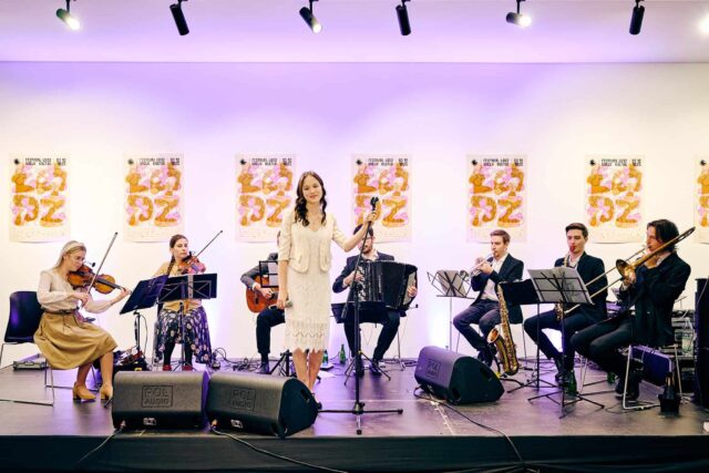 Łódzka Orkiestra Retro, młodzi ludzie z instrumentami, w centrum kobieta w jasnej sukience