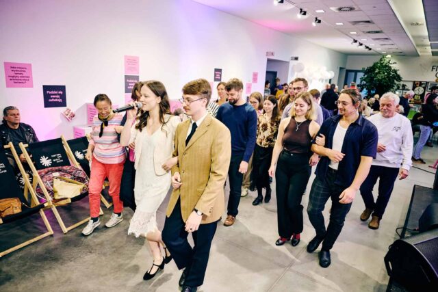 Ludzie tańczą w parach, na czele osoby z zespołu