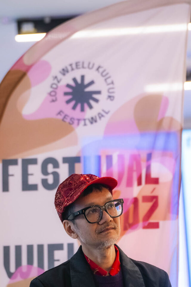 Mężczyzna wietnamczyk w czapce i okularach na tle flagi z napisem Festiwal