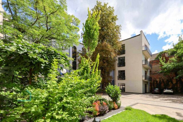 Zadrzewione podwórko, w tle kamienica