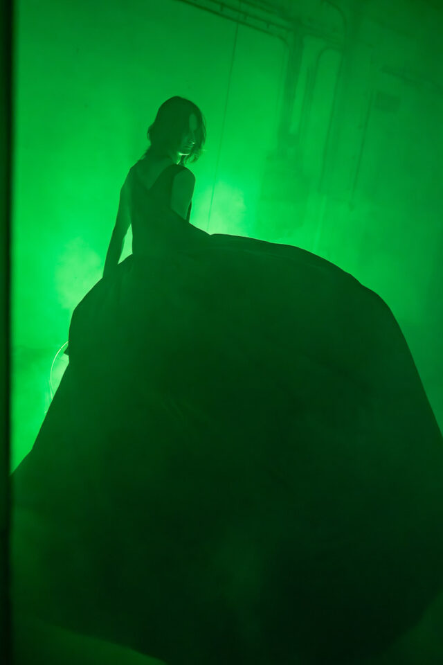 Artysta w ogromnej ciemnej sukni w zielonej przestrzeni