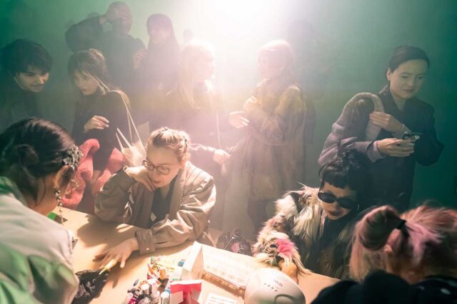 osoby przy stole w trakcie artystycznego manicure, grupa ludzi w tle