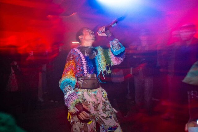 Męzczyzna w kolorowym stroju śpiewający do mikrofonu, w tle publicznośc