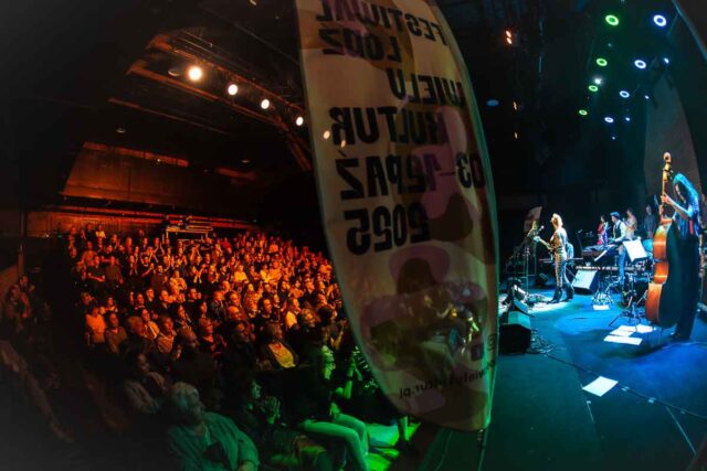 po prawej scena, z muzykami, po lewej widownia, w centrum flaga reklamowa