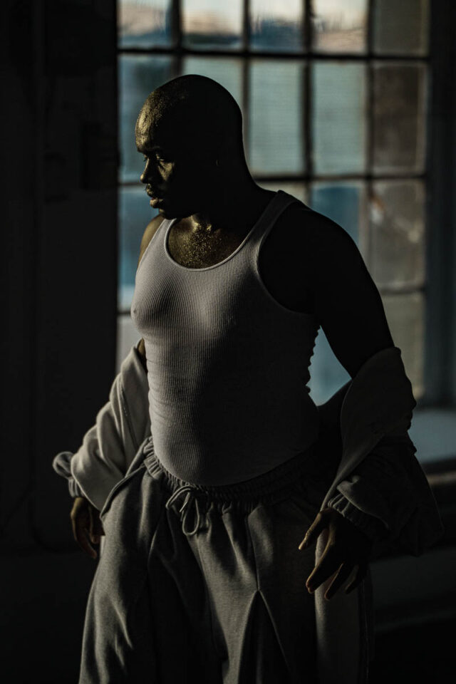 Mężczyzna w białym podkoszulku na tle okna fabrycznego