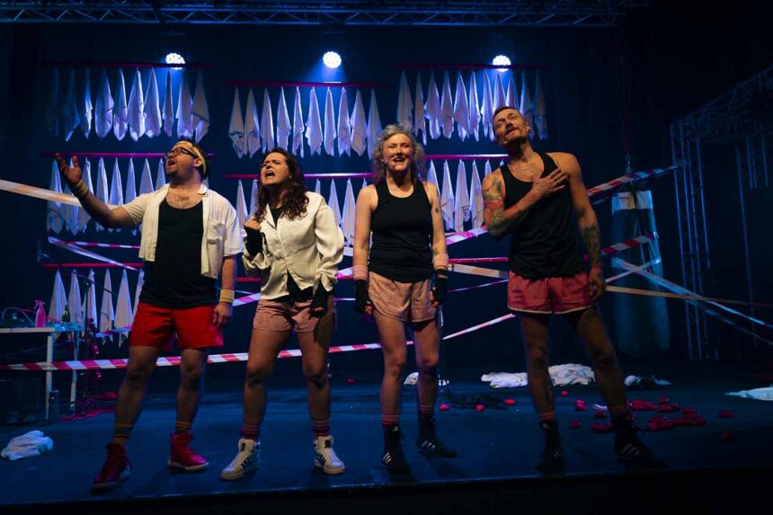 4 osoby na scenie w sportowych strojach, w tle scenografia z ręczników.