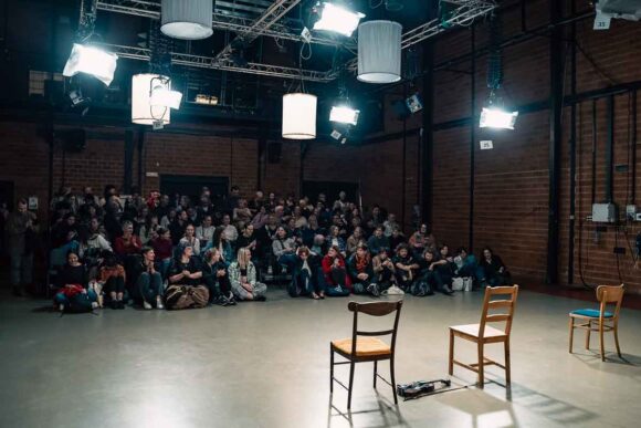 duża sala z pełną widownią, na pierwszym planie na scenie dwa puste krzesła tyłem